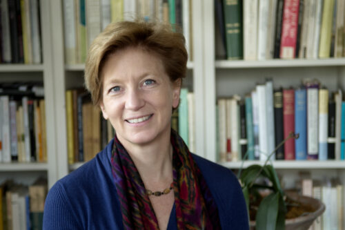 Translator Tess Lewis in smiling front of well-stocked bookshelves