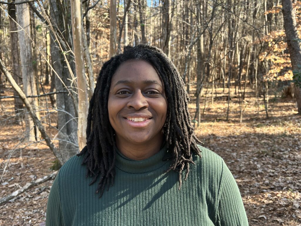 Translator Priscilla Layne, a Black woman with shoulder-length locks, standing in an autumn forest