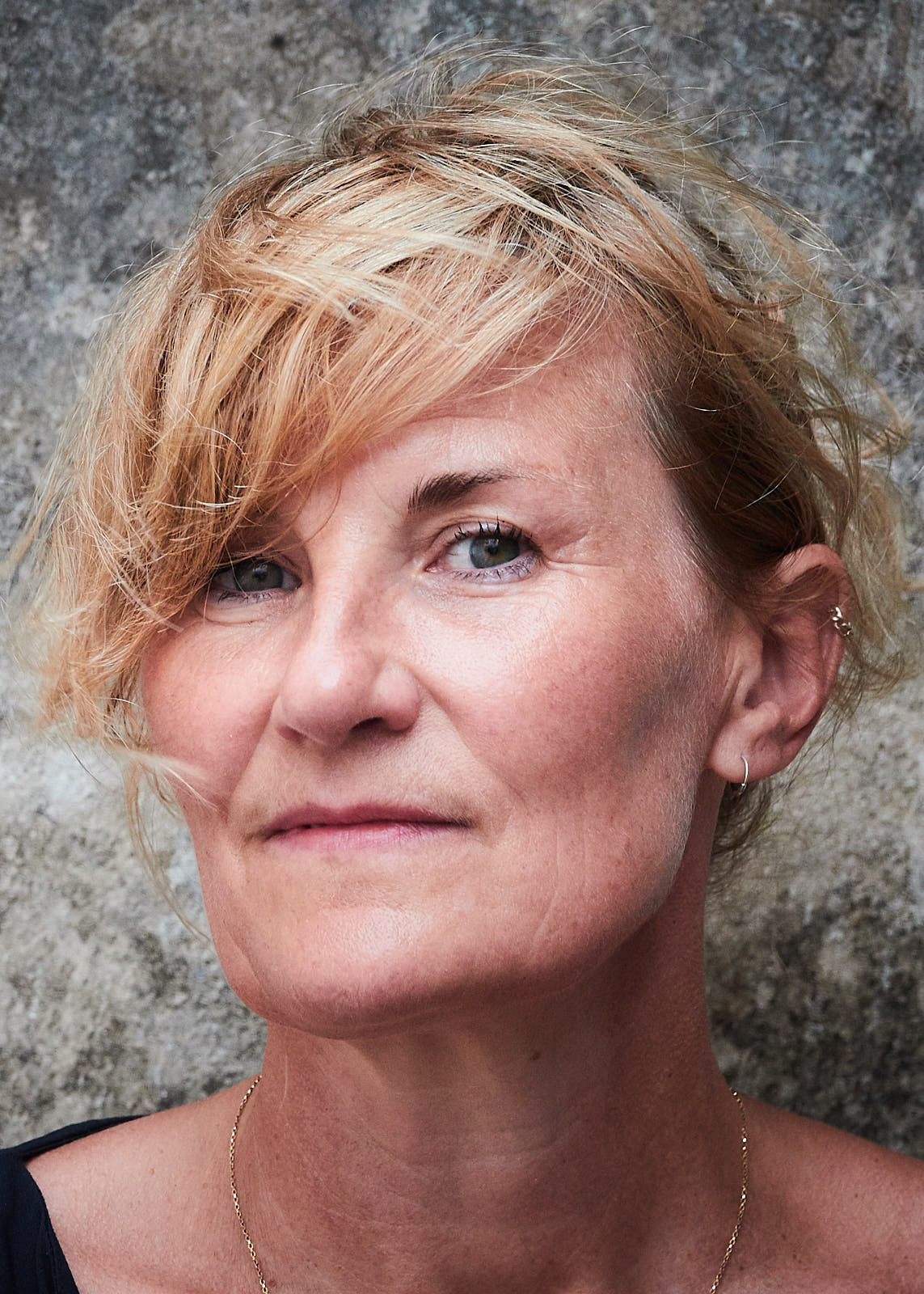 A head shot of translator Lucy Jones, a white woman with a gorgeous blond tangly fringe, in front of a stippled grey wall